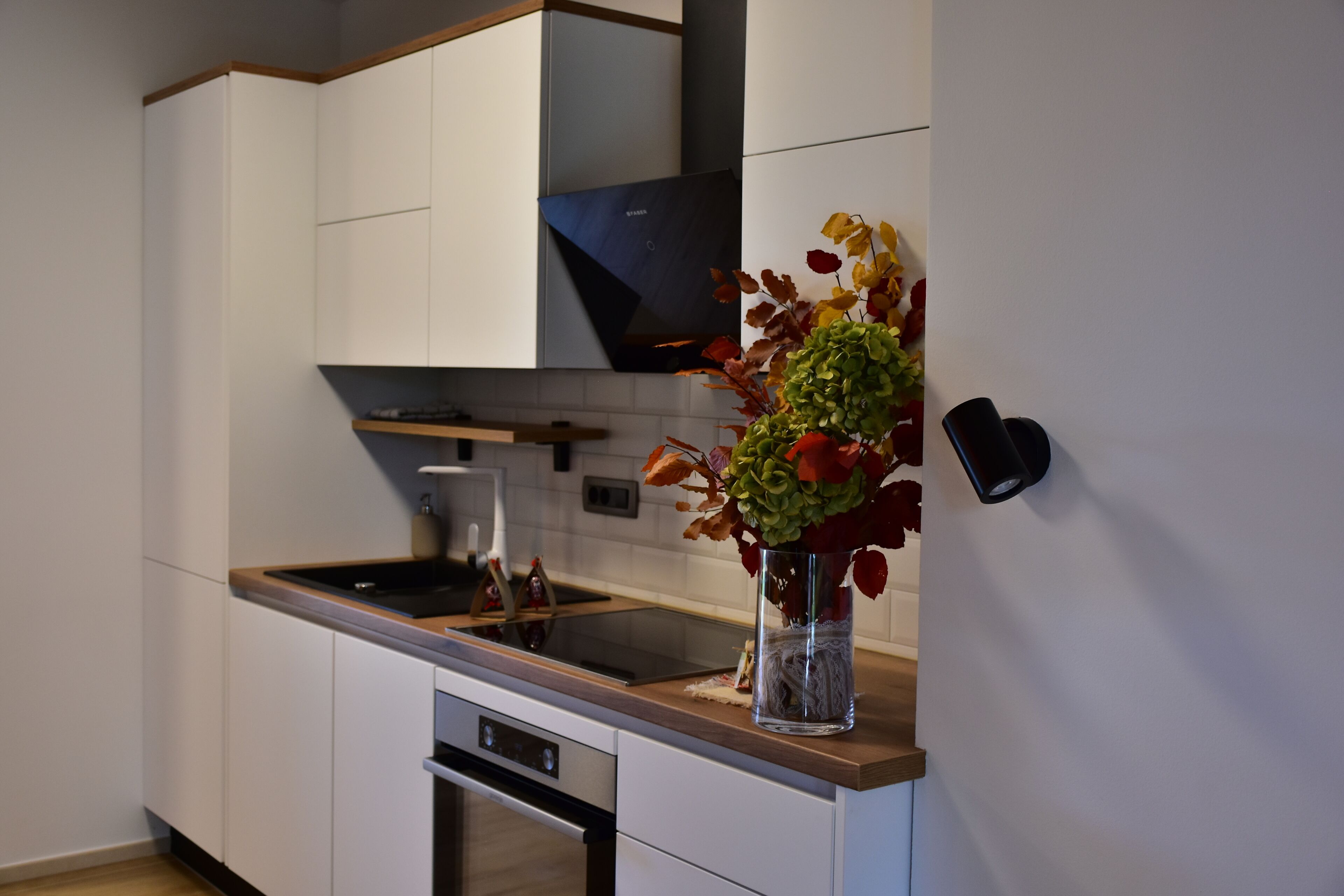 Een moderne keuken met witte kasten, een zwart fornuis en een vaas met bloemen op het aanrecht.