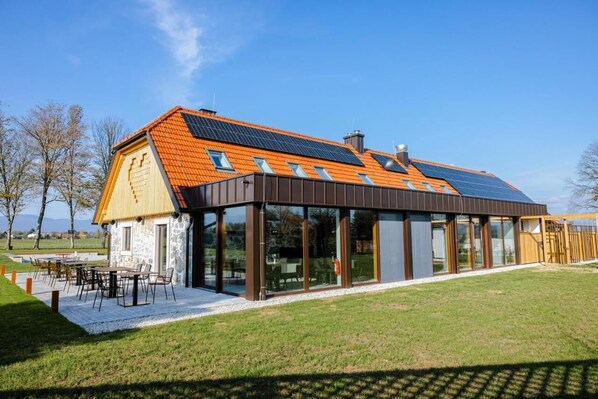 Un edificio moderno con techo inclinado, ventanas amplias y un patio con mobiliario exterior.