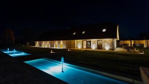 A modern building with a well-lit exterior, a swimming pool, and a patio area. - Resort Village Majer - Apartments, Glamping - Slovenia (Gradac)