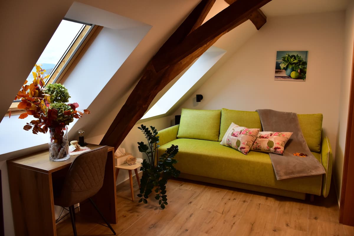 A cozy loft bedroom with a green sofa, a wooden desk, and a large window.