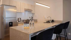 A modern kitchen with a granite countertop, stainless steel appliances, and black bar stools.