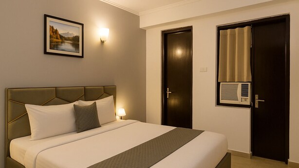 Habitación de hotel con cama, mesita de noche, lámpara de pared, cuadro enmarcado, puerta y ventana con cortinas.