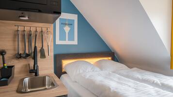 Een moderne hotelkamer met een kitchenette, een bed met witte lakens en een aan de muur hangend schilderij van een toren.