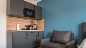 A compact living space with a kitchenette, grey cabinets, a microwave, and a grey sofa. - Antares Apartments (Düsseldorf)