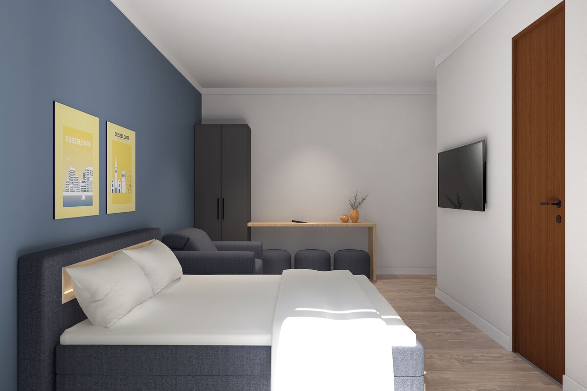 A modern bedroom with a bed, a desk, a TV, and two posters on the wall.