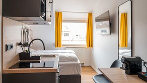 A compact hotel room with a kitchenette, a bed, a dining area, and a large mirror. - Antares Apartments (Düsseldorf)
