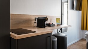 A modern kitchenette with a coffee machine, a small table, and a mirror. - Antares Apartments (Düsseldorf)