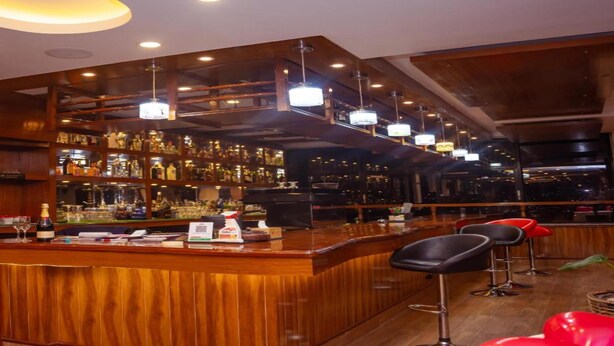 A bar area with wooden shelves stocked with bottles, a counter with bar tools, and red bar stools. - MeroStay 137 Hotel Eye (Lalitpur)