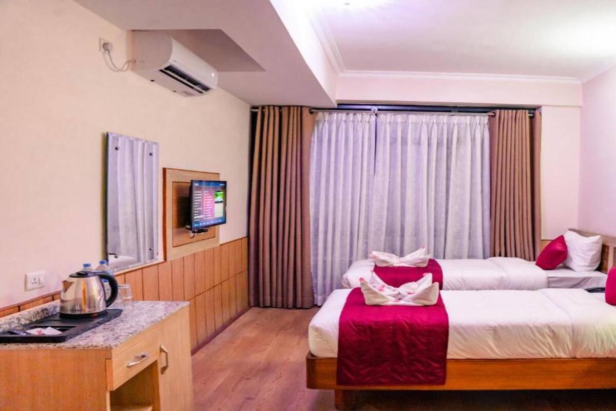 A hotel room with two beds, a desk, a coffee maker, and a TV on the wall.