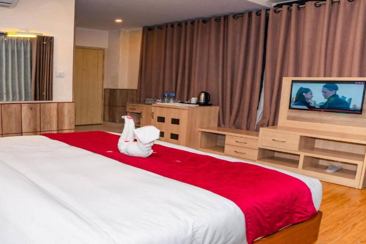 A hotel room with a bed, a TV, a desk, and a red carpet.