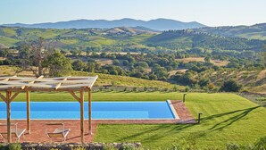 A pool with a pergola and lounge chairs, surrounded by a well-maintained lawn and a view of rolling hills and vineyards. - Villa Grene - Homelike Villas (Grosseto)