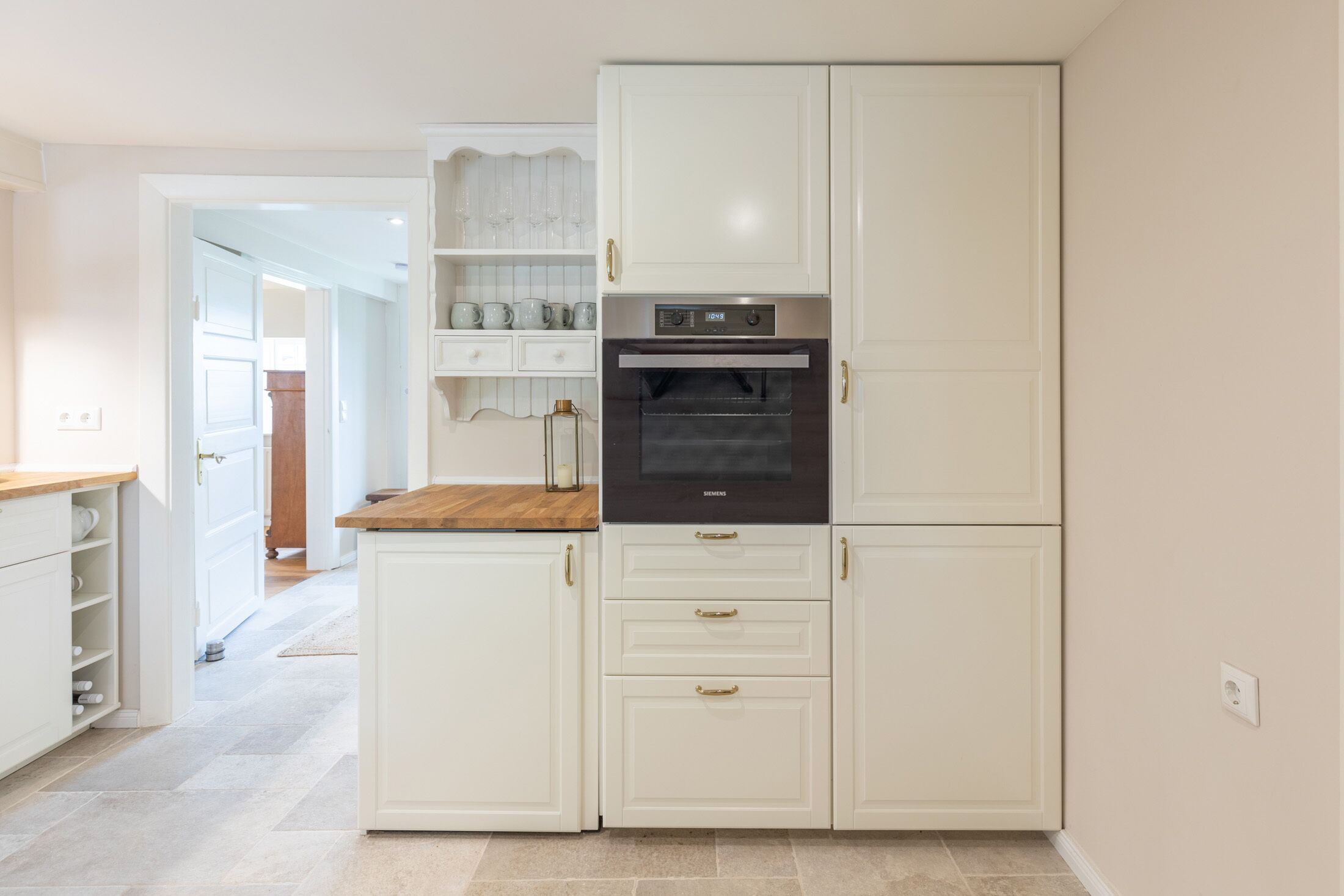 A compact kitchen with white cabinetry, a built-in oven, and a wooden countertop.