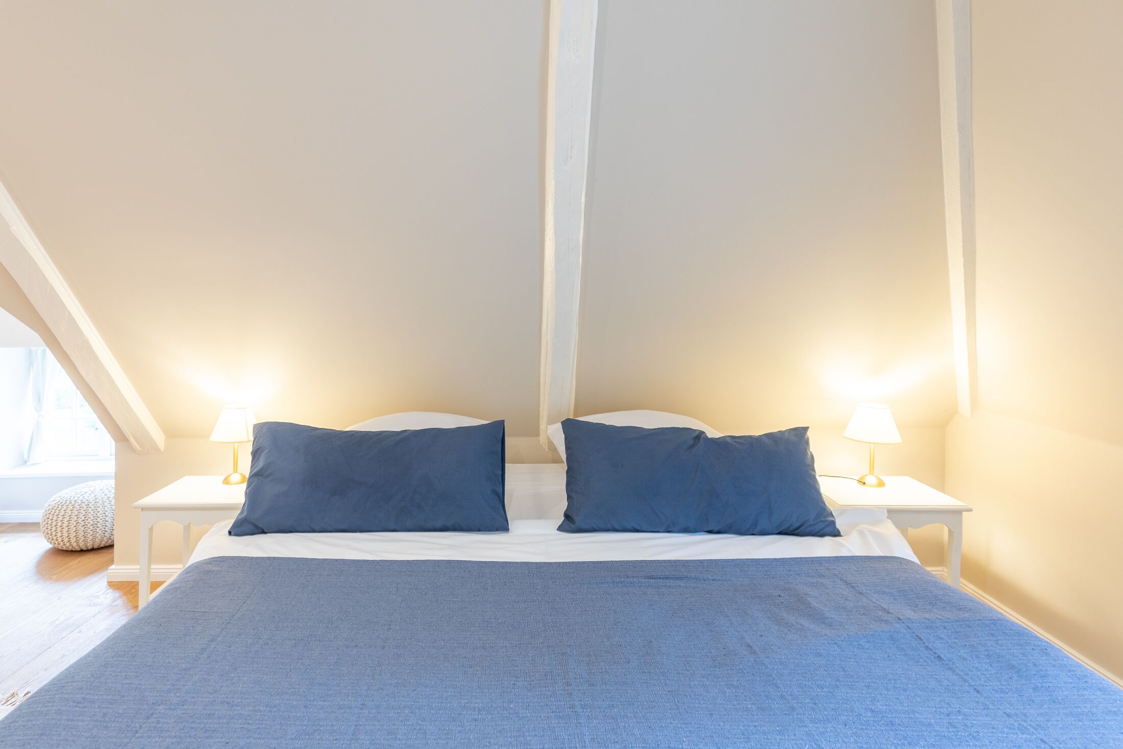 A bedroom with a large bed, two bedside tables with lamps, and a window with curtains.