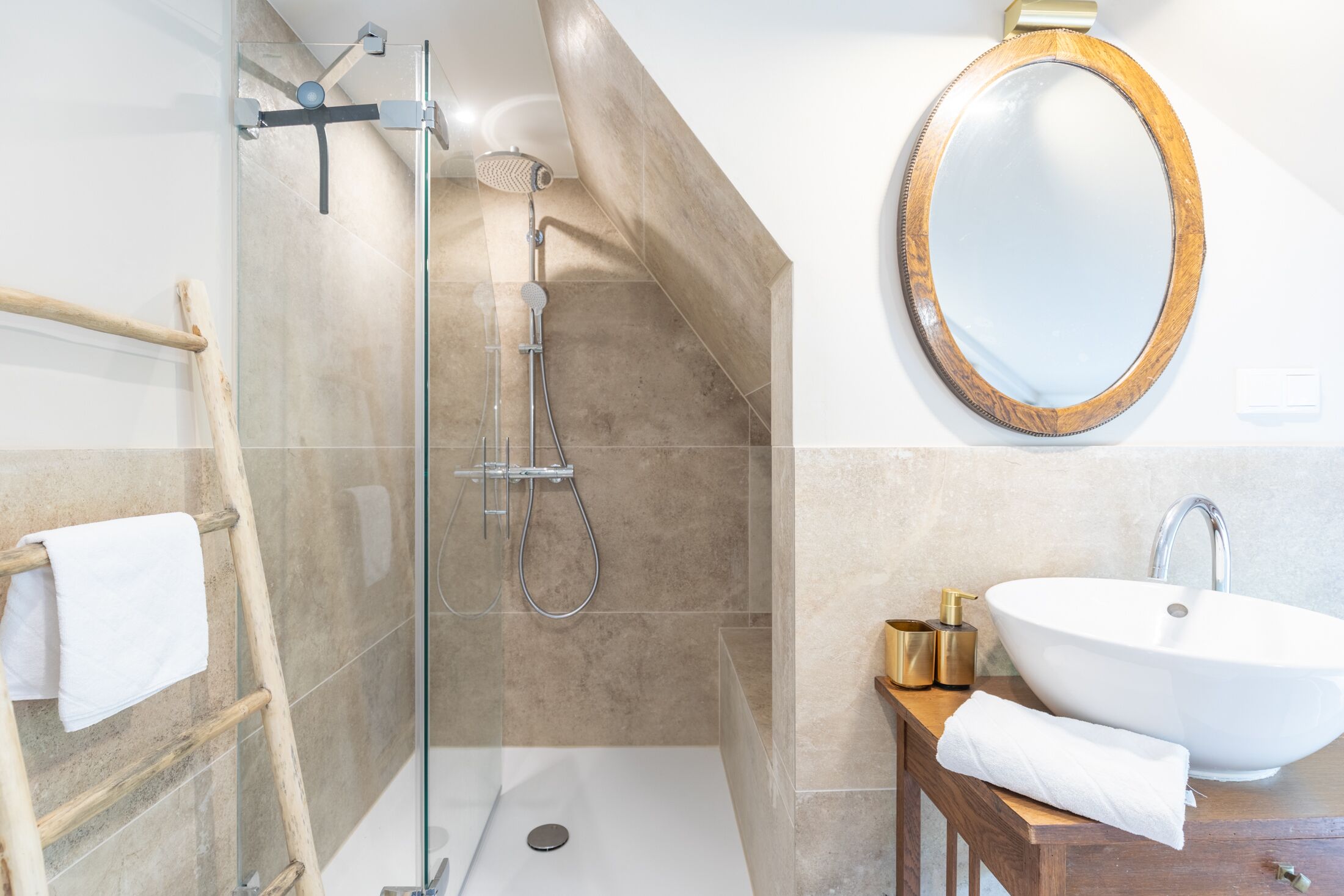 Un baño moderno con ducha de vidrio, tocador de madera con lavamanos y espejo redondo.
