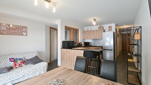 A modern kitchen with wooden cabinets, a microwave, and a refrigerator. There is a dining area with a wooden table and chairs. - Apartment 'Le Barat'ski' with Mountain View, Private Terrace and Wi-Fi (Le Grand-Bornand)