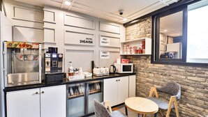 Et moderne køkken med kaffemaskine, brødrister og mikroovn. Der er to stole og et lille bord. Køkkenet har hvide skabe og en murstensvæg.