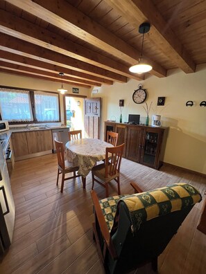A cozy kitchen with wooden beams, a dining table with chairs, a sofa, and a clock on the wall.