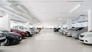 Eine Parkgarage mit mehreren Reihen geparkter Autos, Fliesenböden in Weiß und weißen Decken mit freiliegenden Balken.