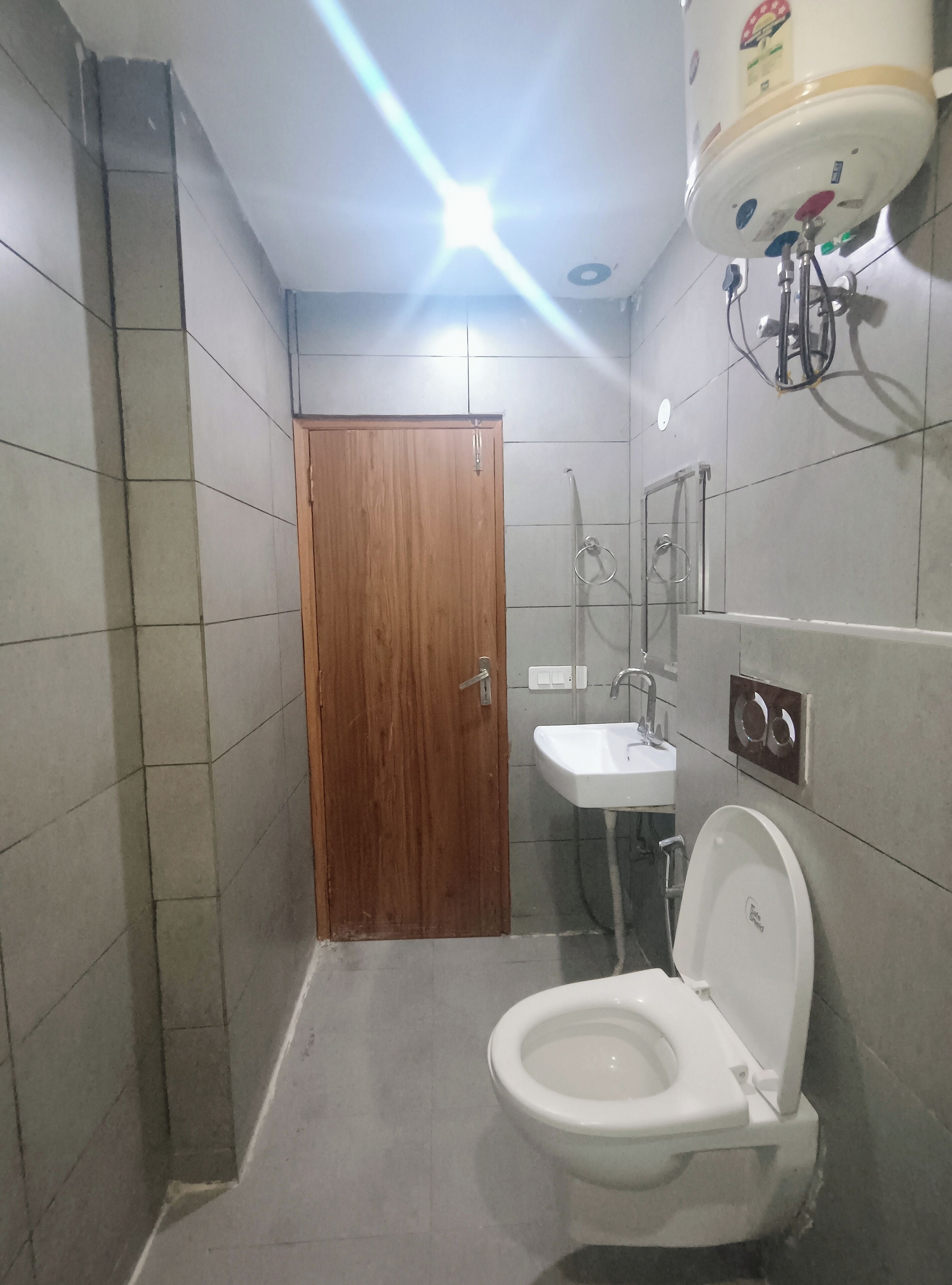 A small, tiled bathroom with a wooden door, a white sink, and a toilet.