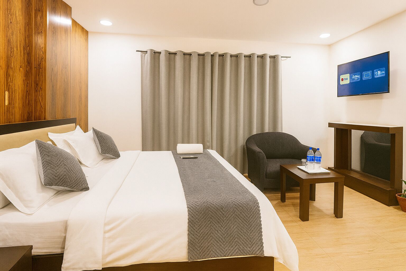 Een hotelkamer met een bed, een stoel, een televisie en een tafeltje met waterflesjes.