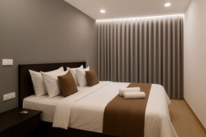 Quarto de hotel moderno com cama bem arrumada, mesa de cabeceira com telefone e uma grande janela com cortinas.