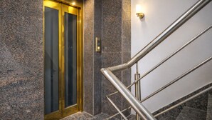 A modern elevator with a metallic finish, a granite-tiled wall, and a metal handrail. - Mauryan Elite Hotel @ Devli Khanpur (New Delhi)
