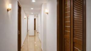 A hotel hallway with wooden doors, white walls, and recessed ceiling lights. - Mauryan Elite Hotel @ Devli Khanpur (New Delhi)