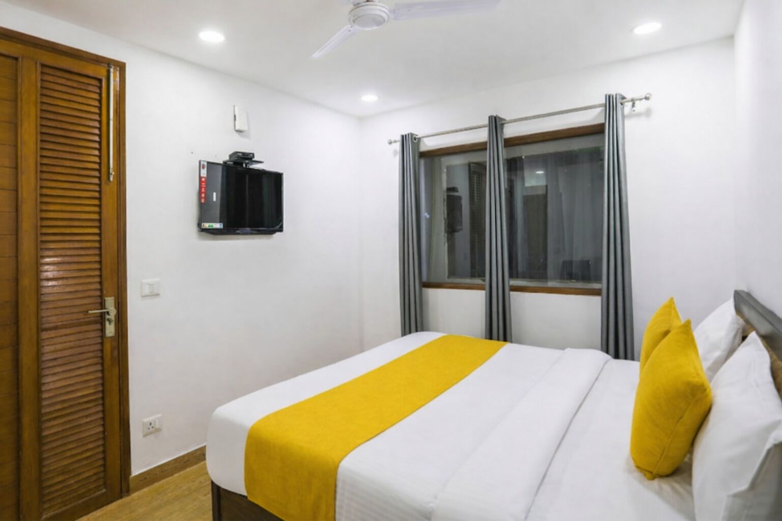 A hotel room with a bed, a television, a window with curtains, and a ceiling fan.