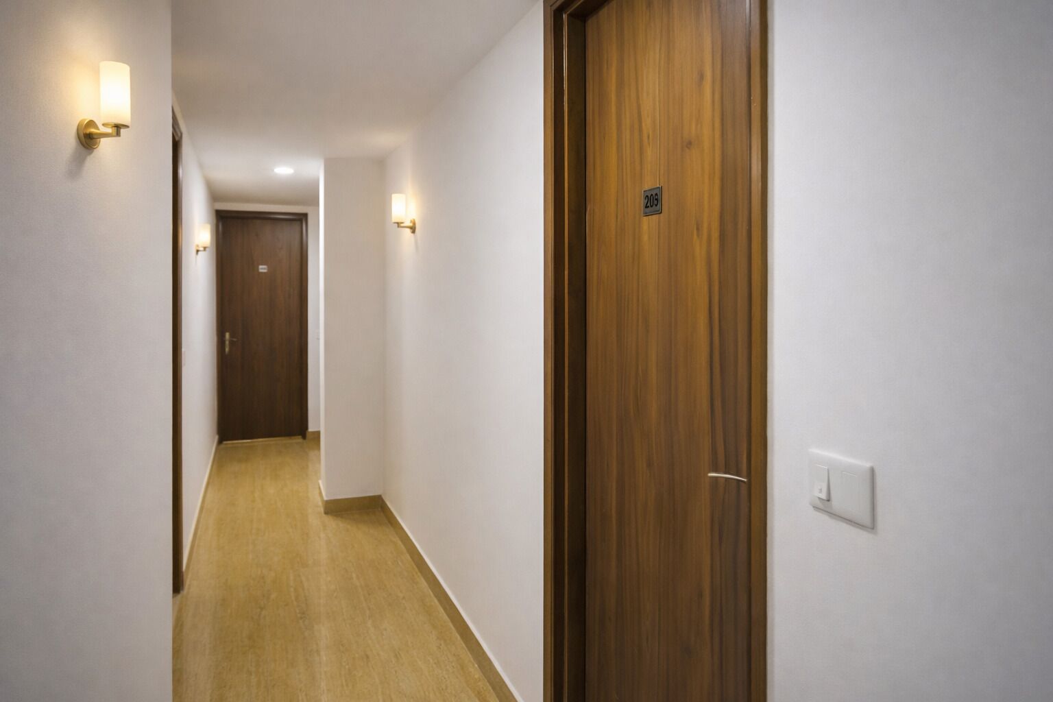 A hallway with wooden doors, white walls, and light fixtures.