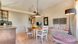 A dining area with a wooden table and white chairs, a stone wall, a sofa with patterned cushions, and a pink ottoman. - When heritage, art and well-being meet (CANDES SAINT MARTIN)