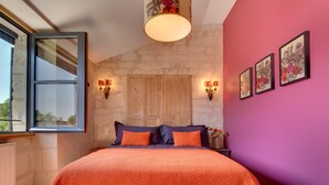 A bedroom with a stone wall, a wooden door, a bed with orange bedding, and wall-mounted lights. - When heritage, art and well-being meet (CANDES SAINT MARTIN)