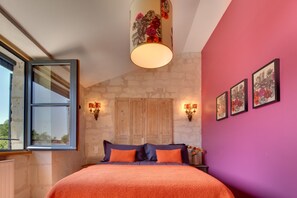 Ein Schlafzimmer mit Steinsturz, Holztür, einem Bett mit orangefarbener Bettwäsche und Wandleuchten.