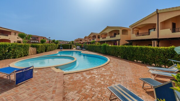 A swimming pool with lounge chairs, a brick patio, and apartment buildings in the background. - Holiday Apartment 'Casa Vacanze Amarena' with Terrace, Balcony & Shared Pool (olbia)