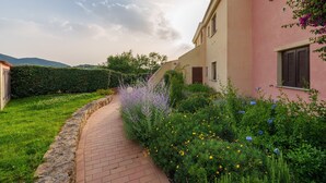 A pathway leading to a building with a pink facade, surrounded by lush greenery and flowering plants. - Holiday Apartment 'Casa Vacanze Amarena' with Terrace, Balcony & Shared Pool (olbia)