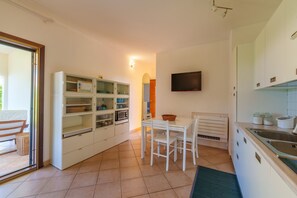 A kitchen with white cabinets, a dining table with chairs, a TV mounted on the wall, and a sliding glass door leading to an outdoor area.