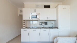 Een kleine keuken met witte kastjes, een magnetron en een koelkast.