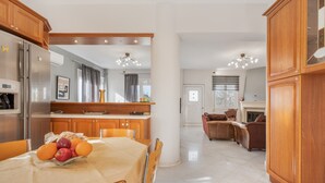 A modern kitchen with wooden cabinets, a dining table with a fruit bowl, and a living area with a fireplace. - Palailimnos Apartment with Sea View, Wi-Fi, and Air Conditioning (Palelimnos)