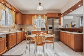 A modern kitchen with wooden cabinets, a dining table with chairs, a refrigerator, and a microwave. - Apartment 'Palailimnos' with Sea View, Wi-Fi and Air Conditioning (Palelimnos)
