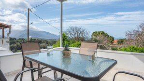 A glass-top table with chairs, a potted plant, and a candle on a balcony with a view of mountains and trees. - Palailimnos Apartment with Sea View, Wi-Fi, and Air Conditioning (Palelimnos)