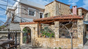 A stone building with a tiled roof, a balcony with potted plants, and a metal gate. - Palailimnos Apartment with Sea View, Wi-Fi, and Air Conditioning (Palelimnos)