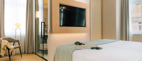 Una habitación de hotel moderna con una cama grande, un televisor de pantalla plana montado en la pared, una silla y una lámpara de pie.
