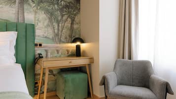 Une chambre à coucher avec un lit, un bureau avec une lampe, un pouf vert et un fauteuil gris.