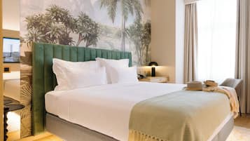 A neatly made bed with a green headboard, white bedding, and a decorative throw. A television is mounted on the wall to the left, and a window with curtains is visible to the right.
