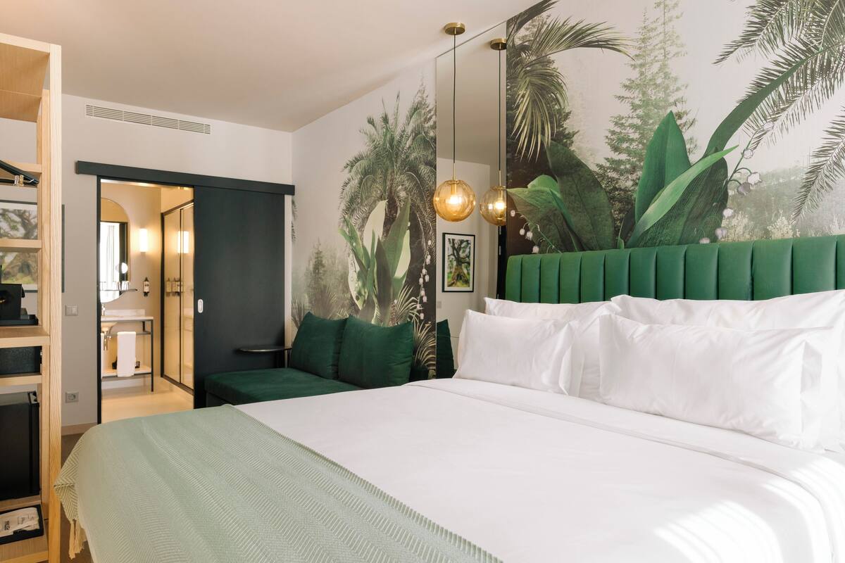A bedroom with a bed, green headboard, and a mural of tropical plants.