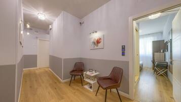 Una habitación de hotel moderna con piso de madera, dos sillas marrones a rayas, una pequeña mesa con lámpara y un cuadro en la pared.