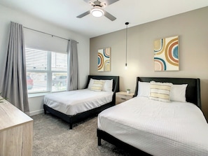A hotel room with two beds, a ceiling fan, a window with curtains, and abstract wall art.