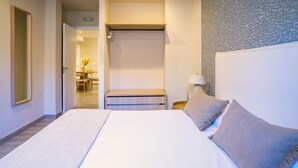 Une chambre d’hôtel avec un lit, une table de chevet avec une lampe, une armoire et une salle de bain visible à travers une porte ouverte.
