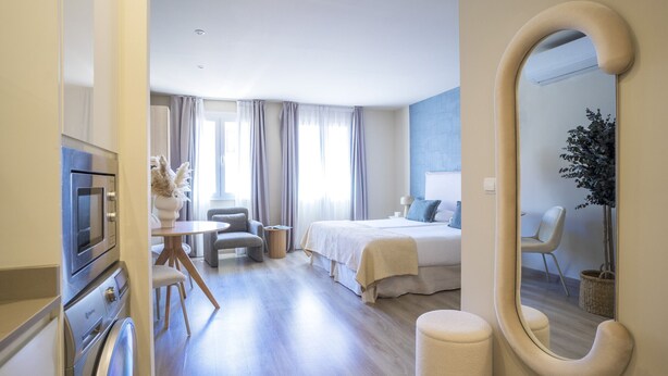 Una habitación de hotel moderna con cama, mesita de noche, silla y un espejo grande.