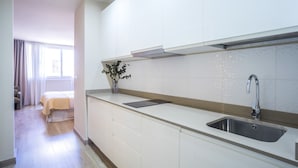 A modern kitchen with white cabinets, a stainless steel sink, and a window with curtains. - Housing Atarazanas by Sharing Co (Málaga)