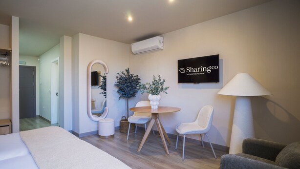 A modern hotel room with a bed, a round table with chairs, a mirror, a wall-mounted TV, and a lamp. - Housing Atarazanas by Sharing Co (Málaga)